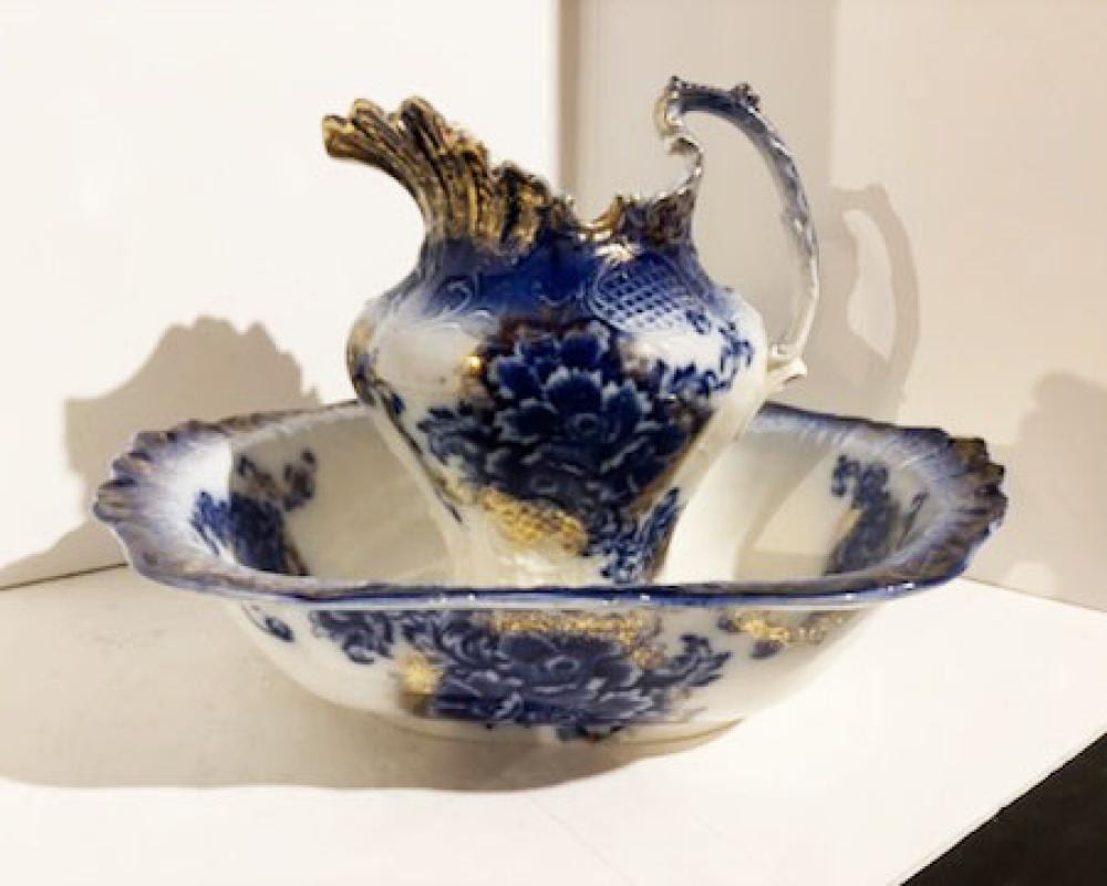 Blue-and-white ceramic pitcher with an ornate spout, sitting in a matching wash basin with floral patterning.