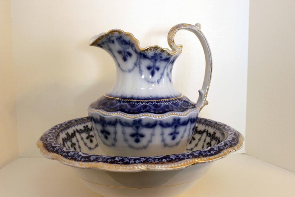 Blue-and-white transfer-printed ceramic pitcher with loop handle resting on a matching oval wash basin.