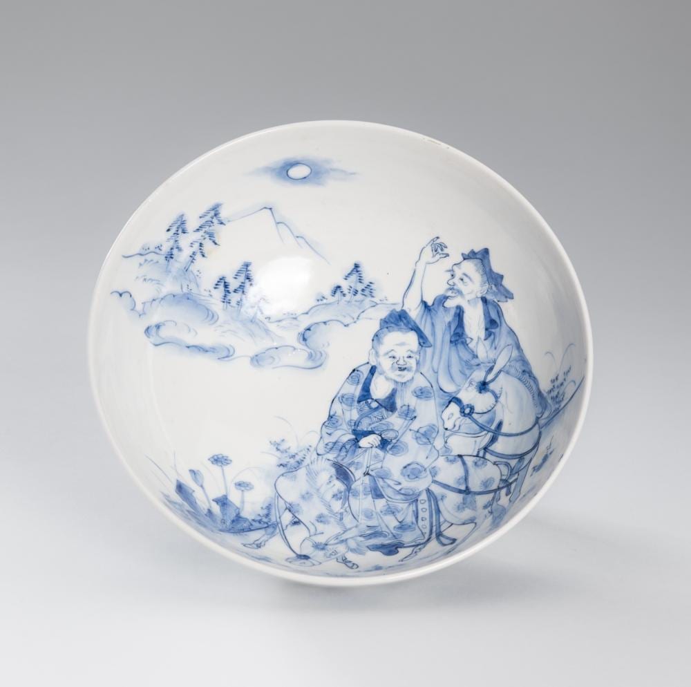Blue-and-white porcelain bowl with illustrated figures and pagoda-like landscape scenes around the interior.
