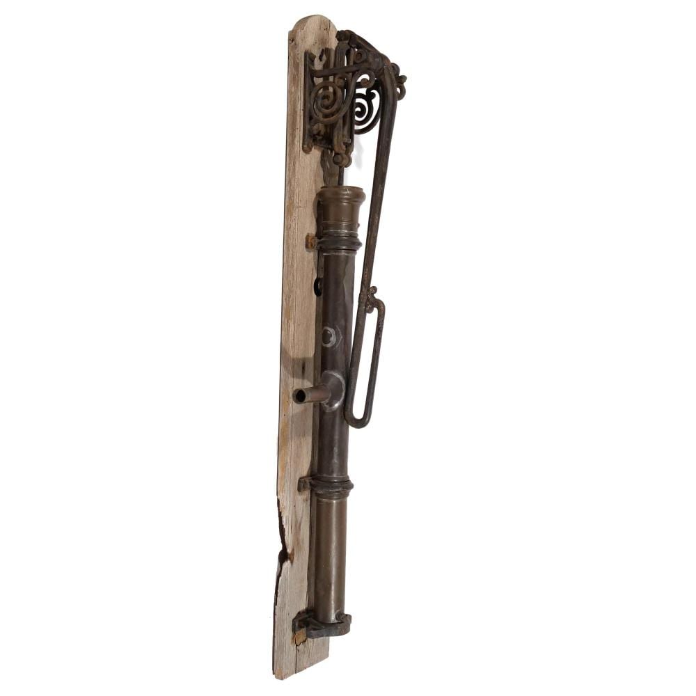 Antique-style hand water pump mounted on a wooden frame with decorative metal scrollwork and a cylindrical metal spout.