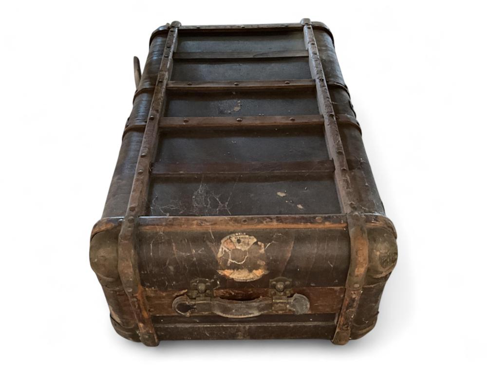 Antique-style leather trunk with metal corner straps, front latch and worn decorative label on the front panel.