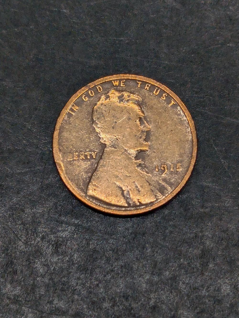 Close-up of a circulated U.S. one-cent Lincoln Wheat penny showing “IN GOD WE TRUST,” “LIBERTY,” and the date “1915.”