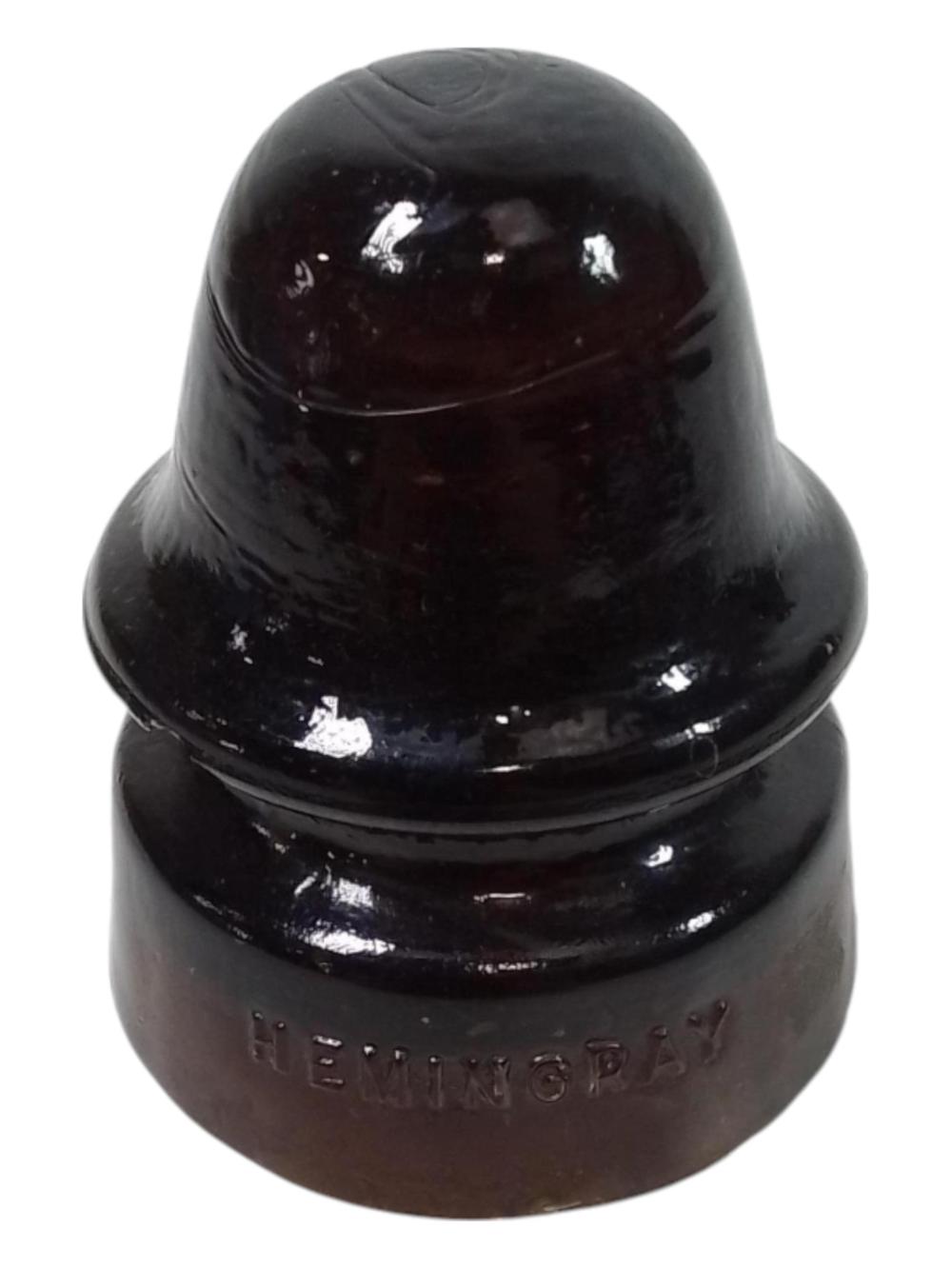 Dark amber glass insulator with a domed top and embossed markings near the base, photographed against a white background.