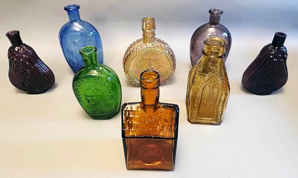 tray box lot of (8) vintage colored glass bottles: (5) flask type; Old Cabin whiskey reproduction; amber, green, blue, amethyst sold by Roan Inc. Auctioneers & Appraisers, lot 36 — auction record photograph
