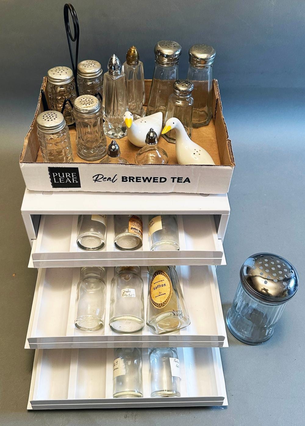 Small kitchen lot: small tray box lot of salt & pepper shakers, sugar shaker, counter top cabinet for spice bottles, with 3-drawers/some bottles sold by Roan Inc. Auctioneers & Appraisers, lot 396 — auction record photograph