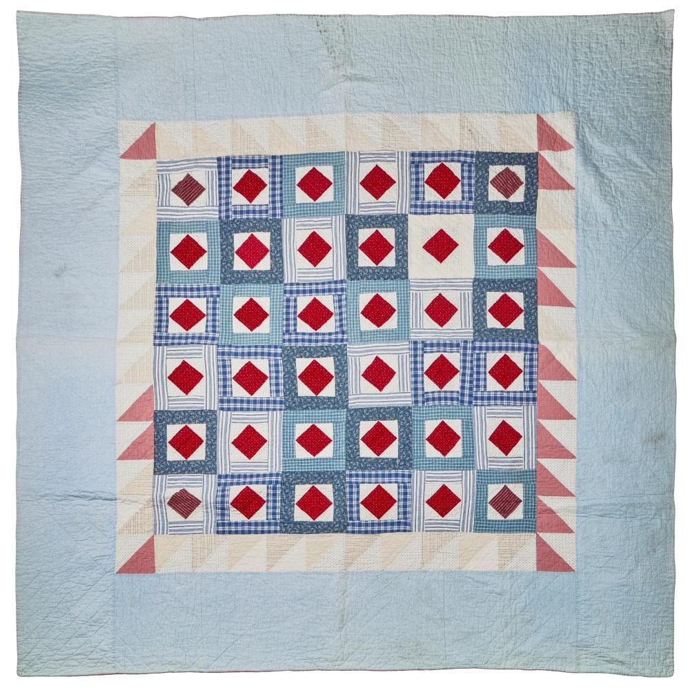 Square patchwork quilt with red diamond shapes and blue plaid blocks, on a light blue background with triangular corner patches.