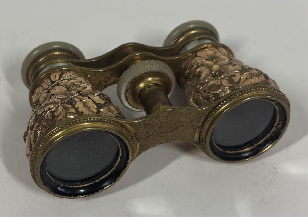 Pair of ornate brass opera glasses with leaf-engraved metal barrels and dark oval viewing lenses.