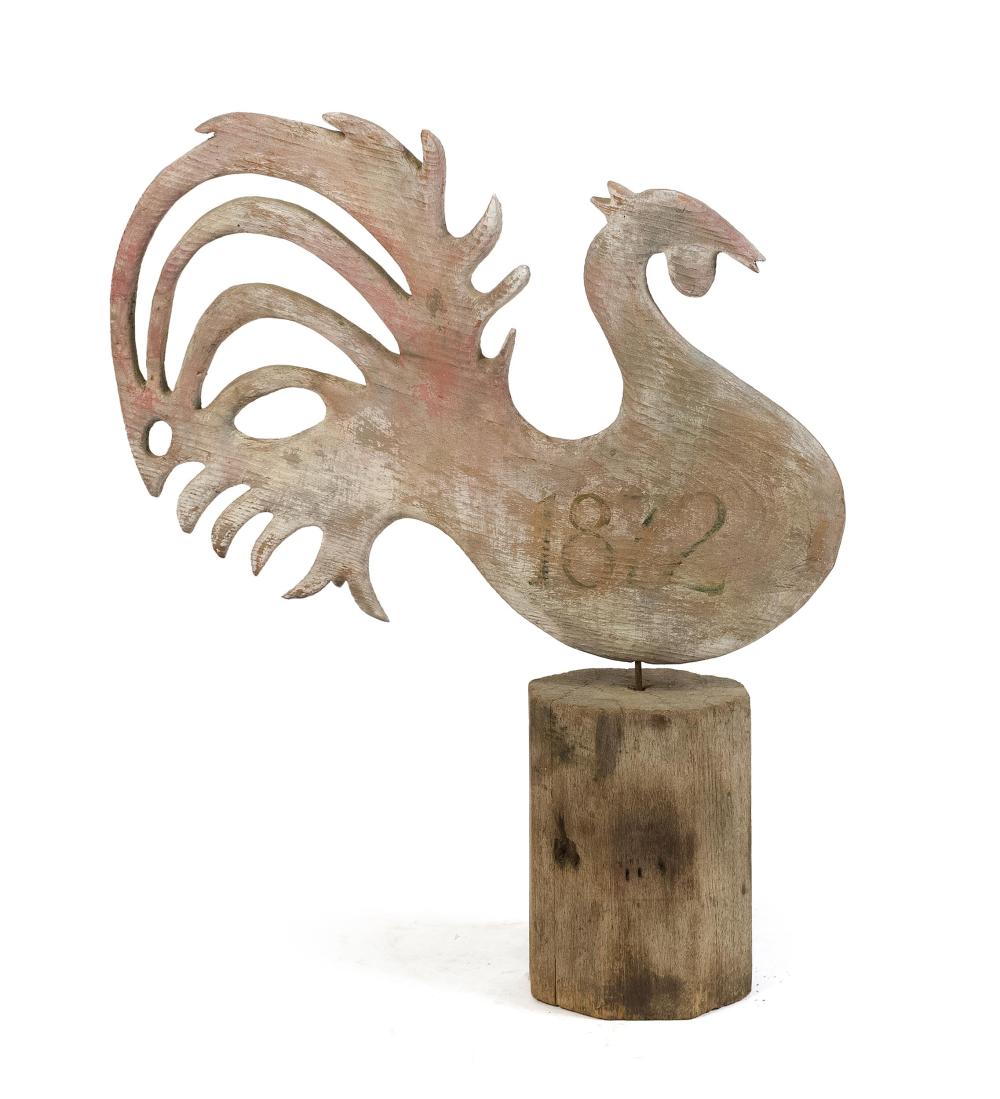 Wooden rooster weathervane with openwork tail and red accents, mounted on a cylindrical wooden base.