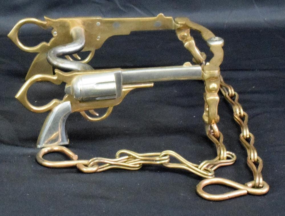 Brass and steel horse curb bit with decorative figural end pieces and attached chain on a dark background.