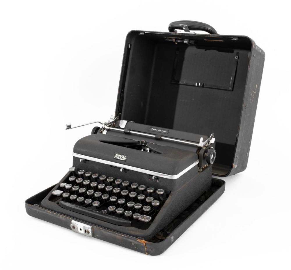 Black portable typewriter with keys visible and lid open, shown in a suitcase-style case.