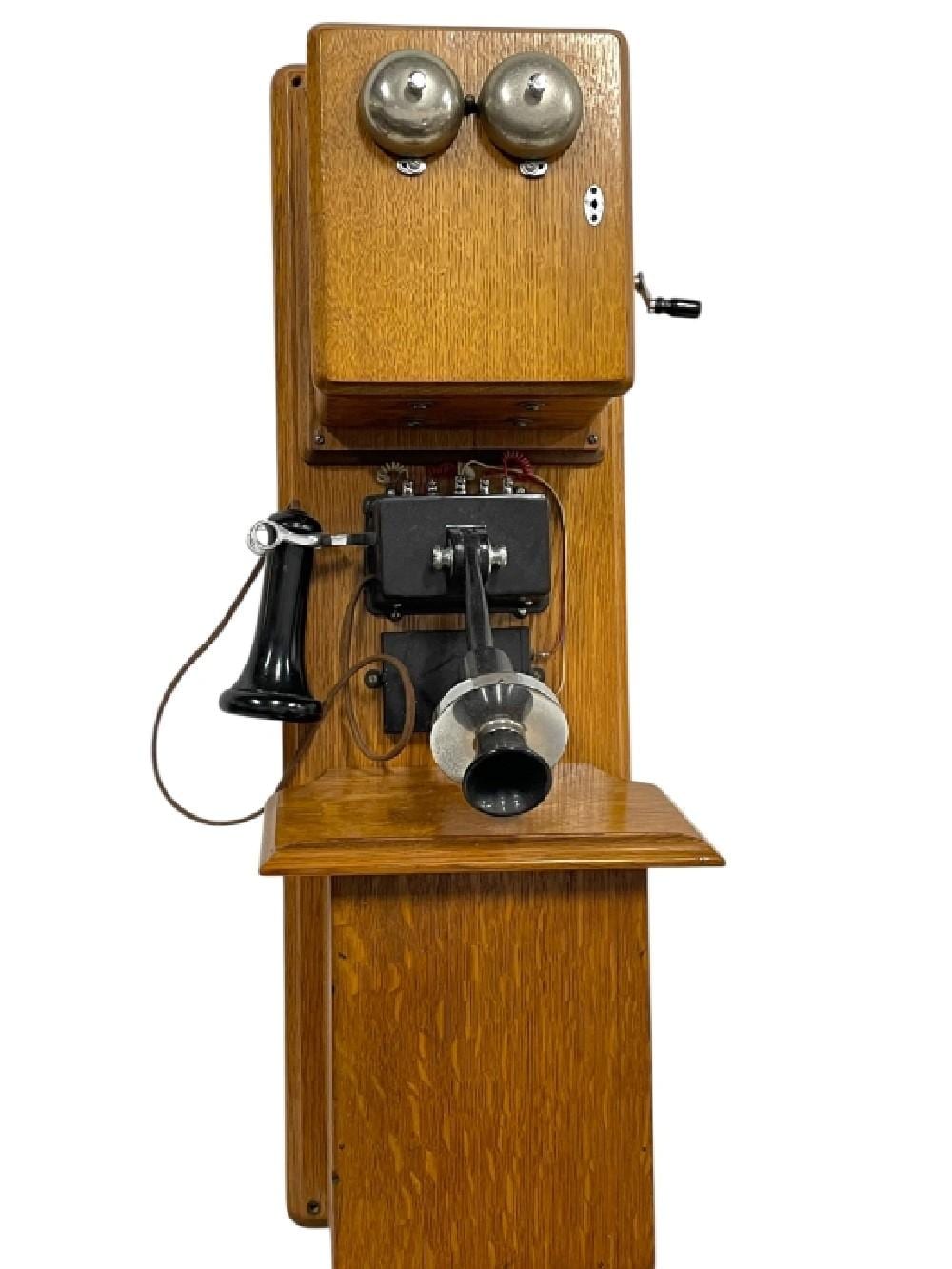 Antique wall-mounted oak telephone with two chrome bells on top, black handset cradle, and a dial/base unit below.