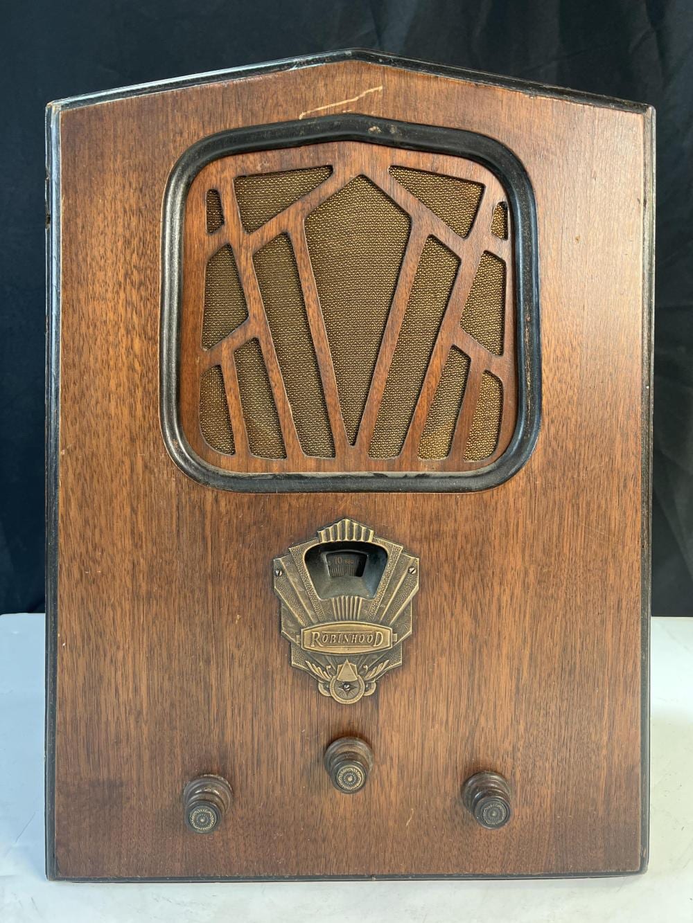 Front view of a wooden vintage radio cabinet with a decorative gold speaker grille, a “Robinhood” badge, and three control knobs.