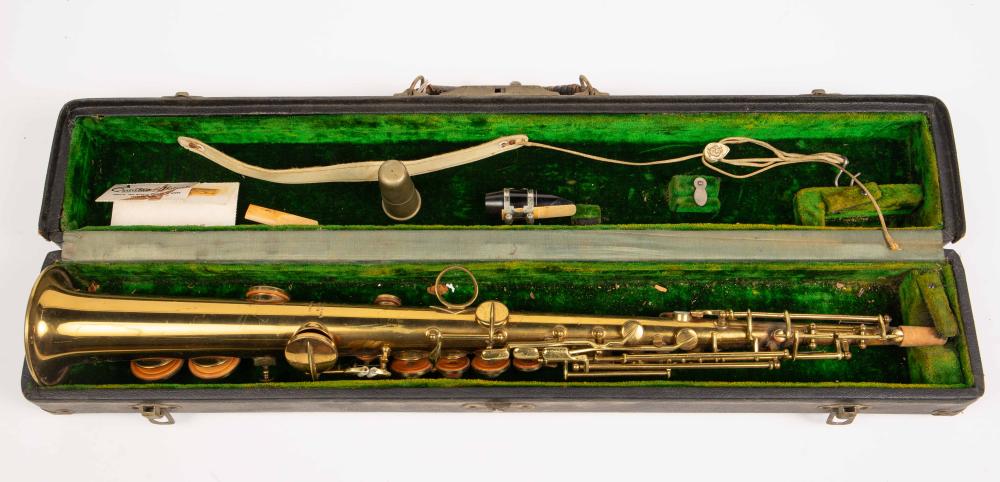 Antique brass soprano saxophone laid inside a green-lined carrying case with accessories across the top.