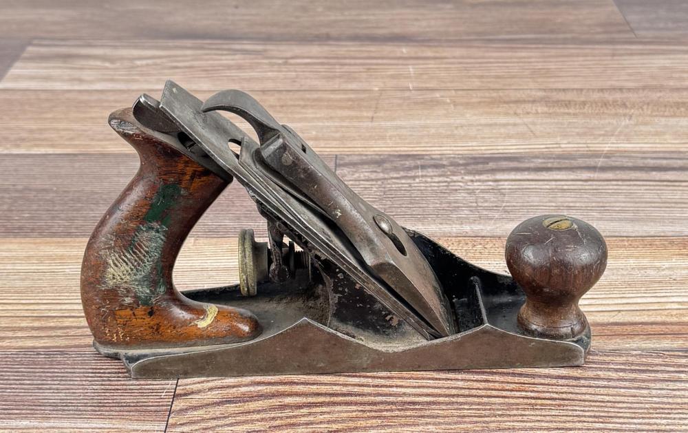 Metal wood plane with a wooden handle and worn finish placed on a striped wooden surface.