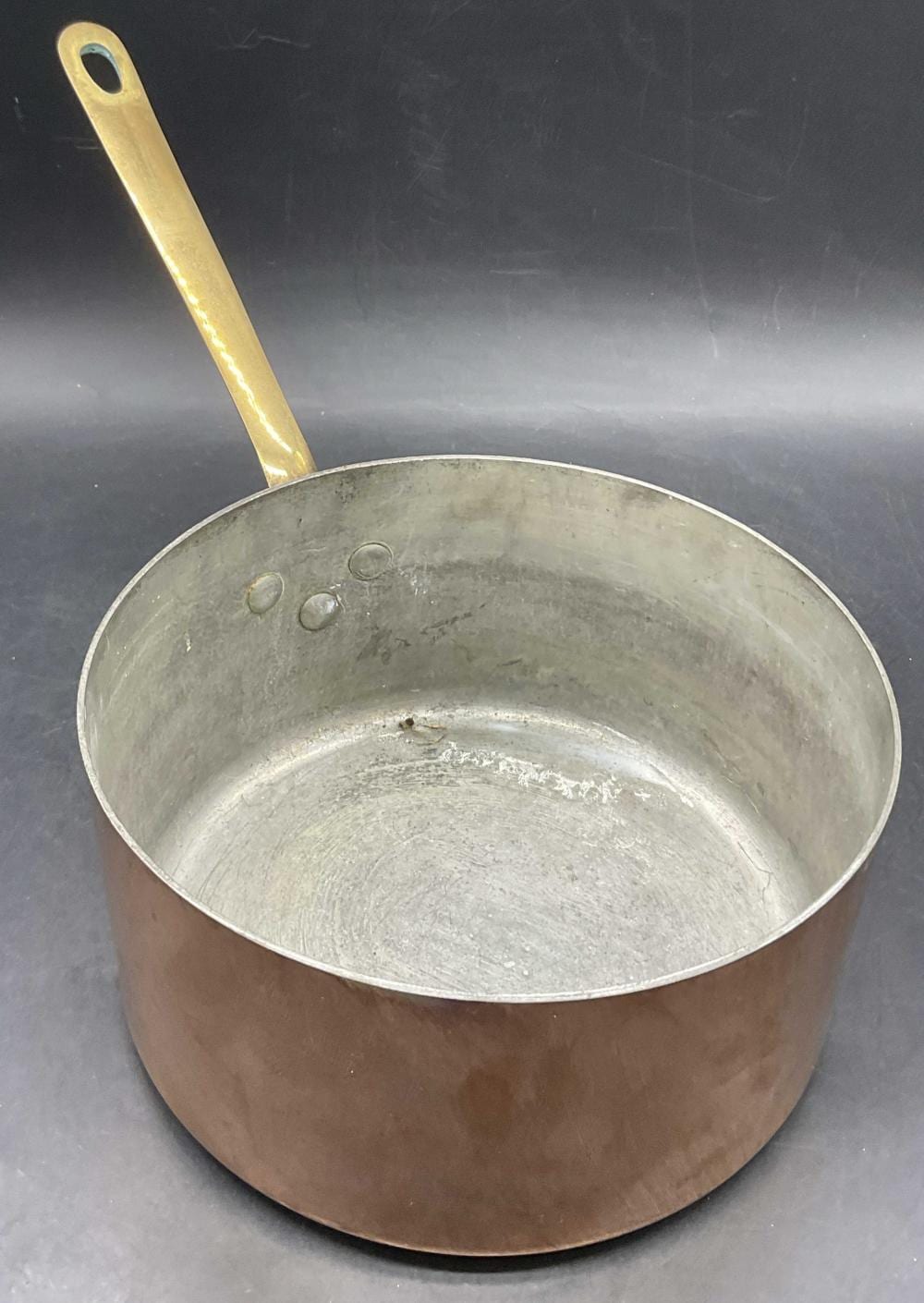 Copper saucepan with a brass handle and a flared rim, viewed from the side over a dark background.