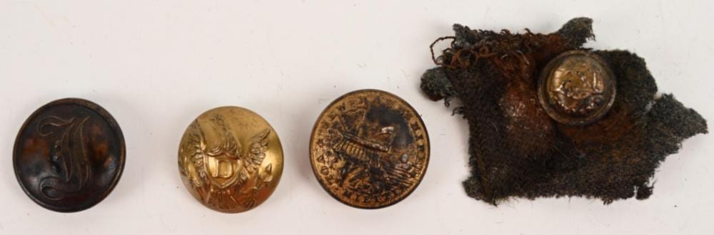 Group of four small metal buttons with stamped designs and a small cloth fragment with a round button attached.