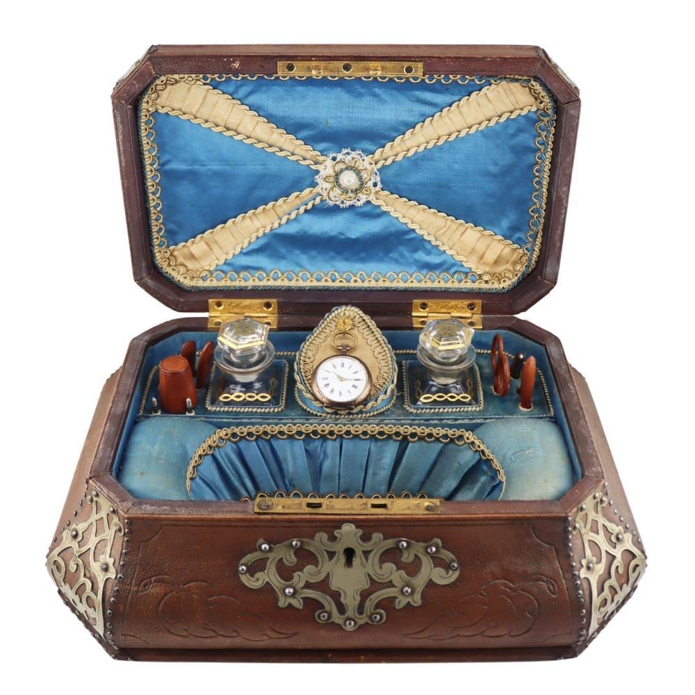 Open brown vintage sewing box with blue fabric lining and brass hardware, showing a small clock and sewing tools inside.
