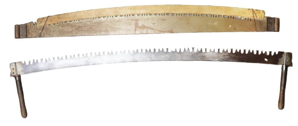 Old hand saw with a long metal blade and teeth, mounted on a wooden frame with two pointed legs for support.