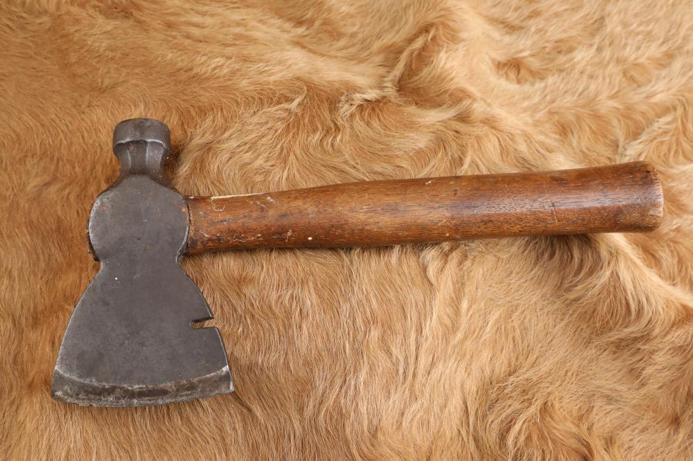 Head and wooden handle of a metal carpenter’s hammer/hatchet lying on a tan fur-like surface.