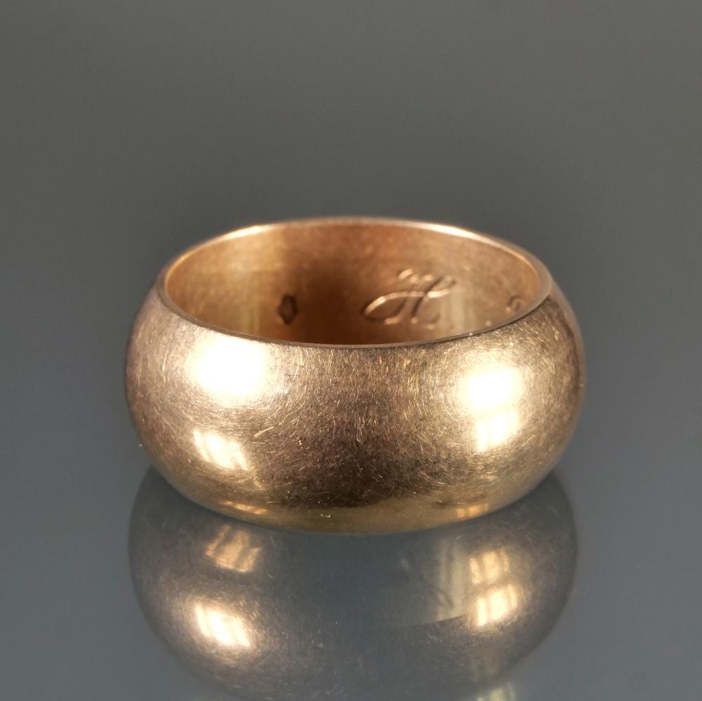 Close-up of a gold band ring with a plain domed top and light engraving inside the band.