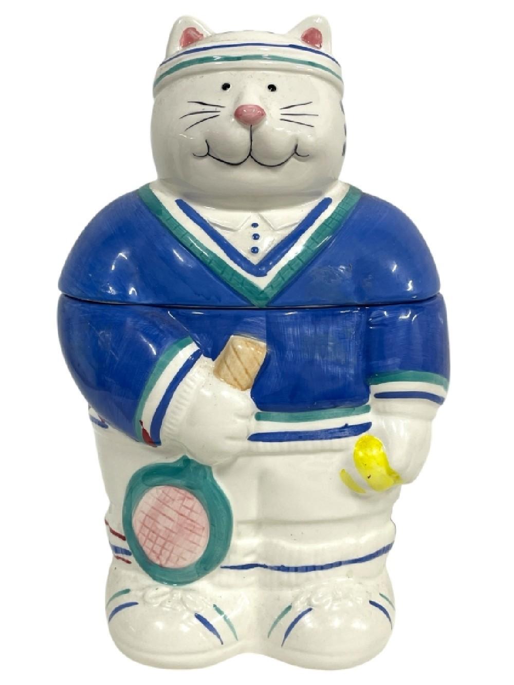 Ceramic cat cookie jar shaped like a tennis player, with a blue outfit, racket, and a smiling face with pink nose.