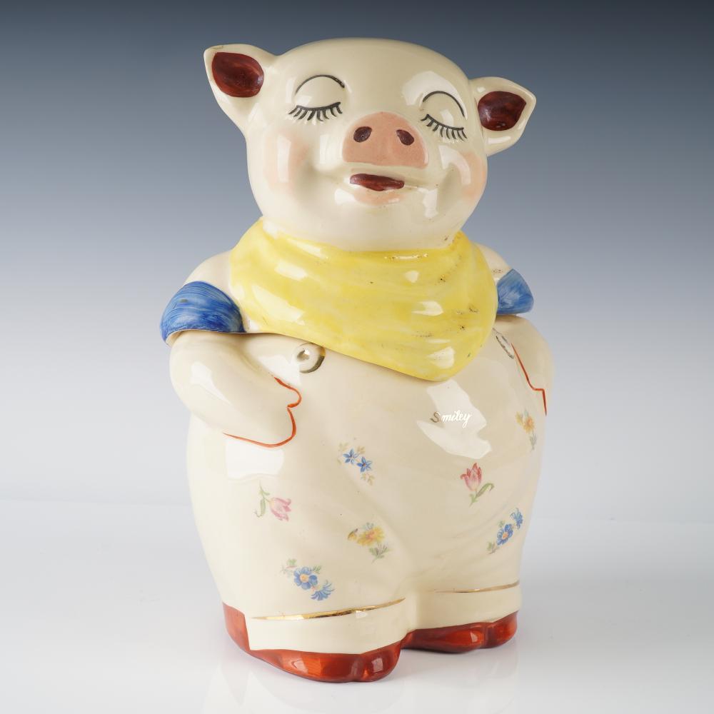 Smiling pig cookie jar with painted eyelids, red ears, yellow scarf, and a hand-painted floral pattern on the body.