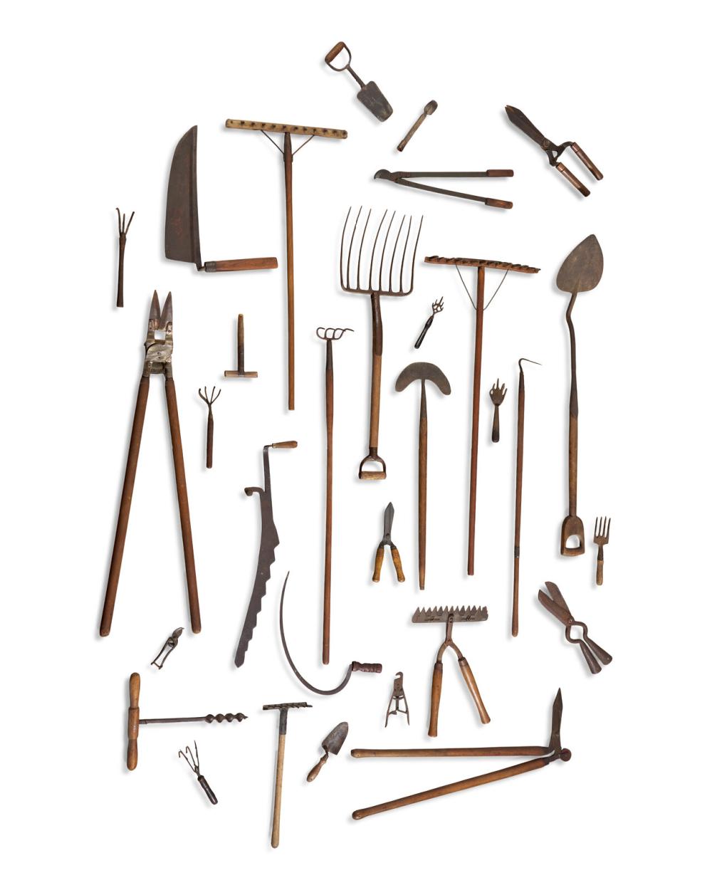 Assorted spread of vintage-style metal and wooden garden tools on a white background, including rakes, shovels, and hand cultivators.