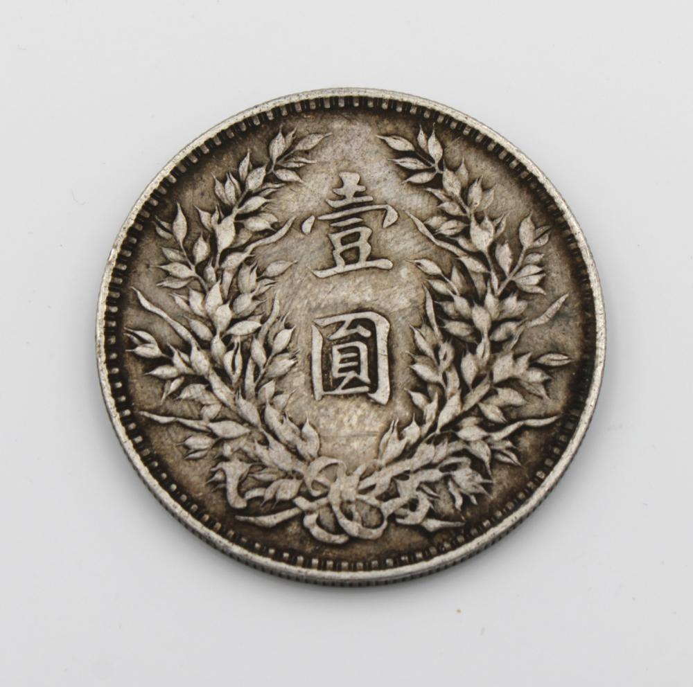 Close-up of a silver-colored coin showing a wreath with Chinese characters in the center and a beaded rim.