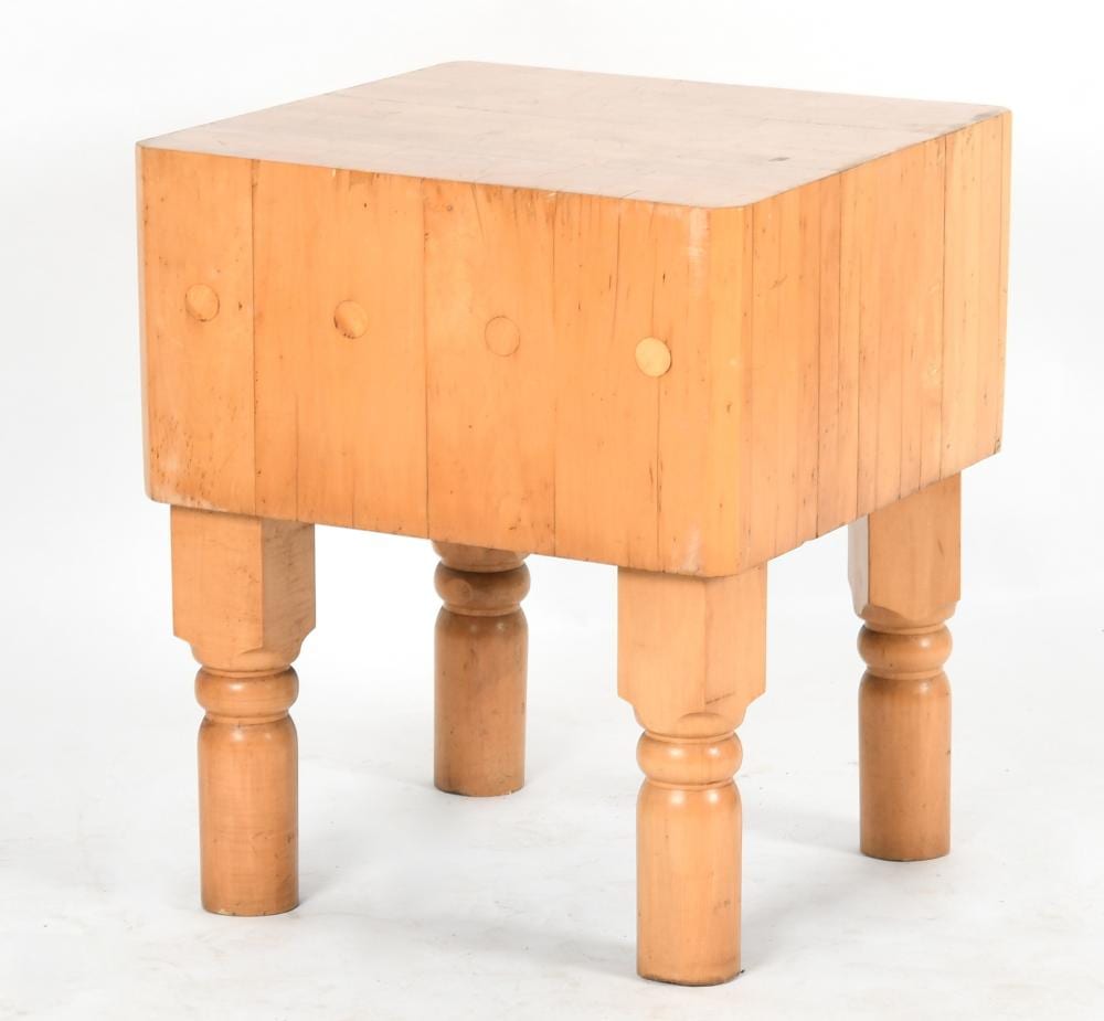 Square wooden butcher block table with a pale top and four turned legs, seen from a three-quarter angle.