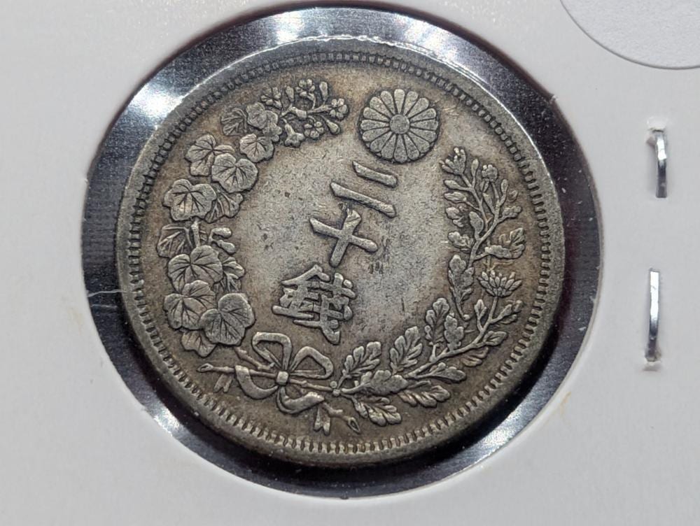 Close-up of a silver Japanese coin showing a central character and floral and sunburst designs around the rim.