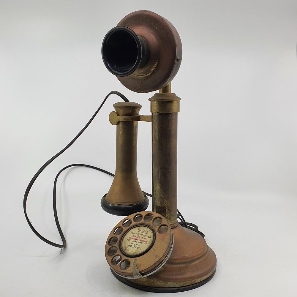 Vintage rotary telephone on a base with brass-colored receiver and handset, black dial and cord, photographed against a plain light background.