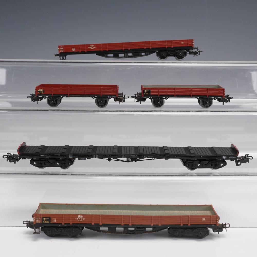Five model train freight cars in red and black on a white display background, including two red boxcars and three flatbed-style cars.
