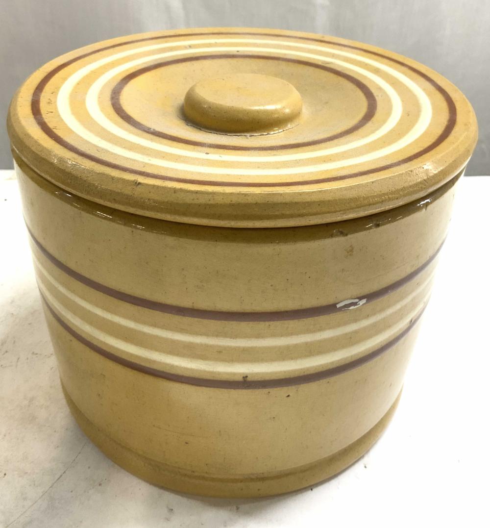 Yellow ceramic butter crock with a domed lid and dark brown and white striped decoration around the sides.