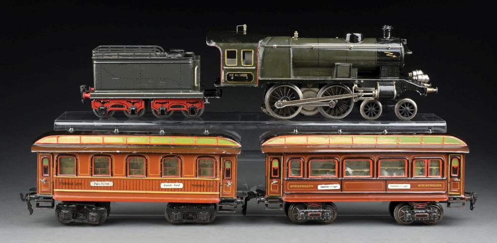 Model train set on a dark background, showing a green steam locomotive with tender and two orange passenger cars.