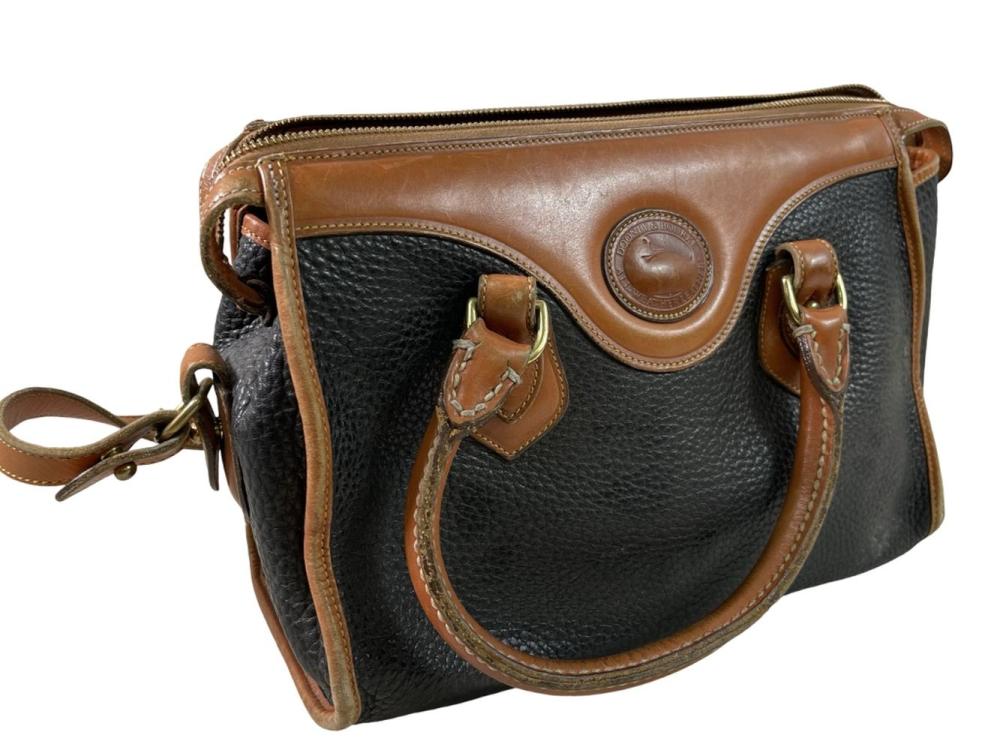 Vintage-style crossbody purse with brown top trim, dark textured front panel, and a round logo medallion on the flap.