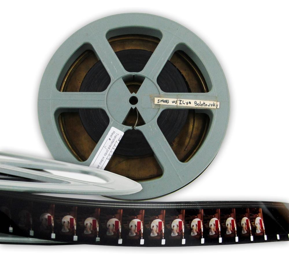 Light blue 16mm film reel with a label and a strip of film coming off, photographed against a white background.