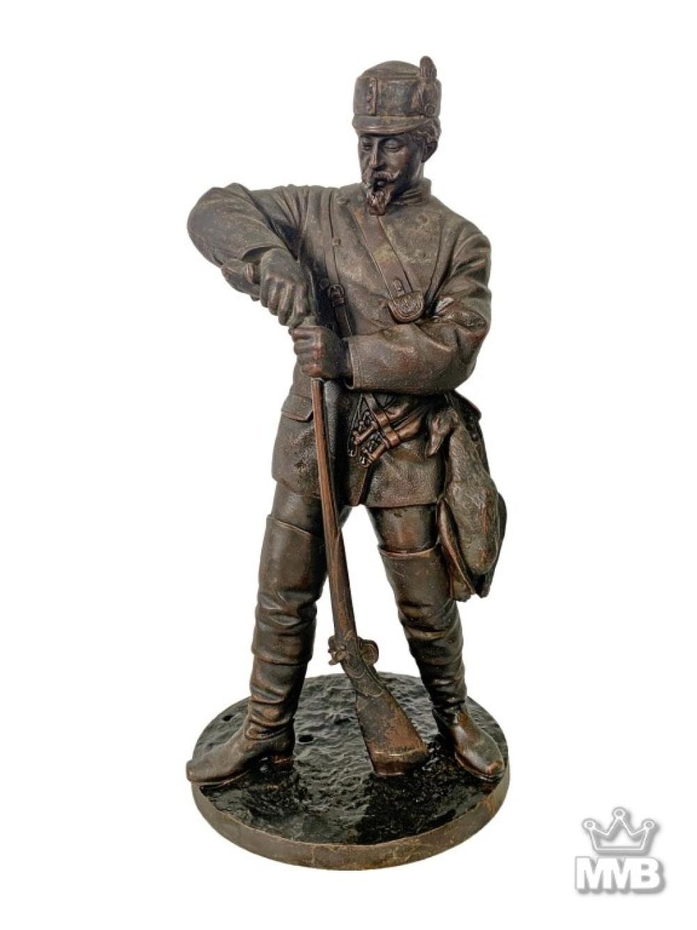 Antique-style bronze-toned soldier sculpture standing with one arm extended holding a long rifle, wearing a helmet and uniform, on a round base.