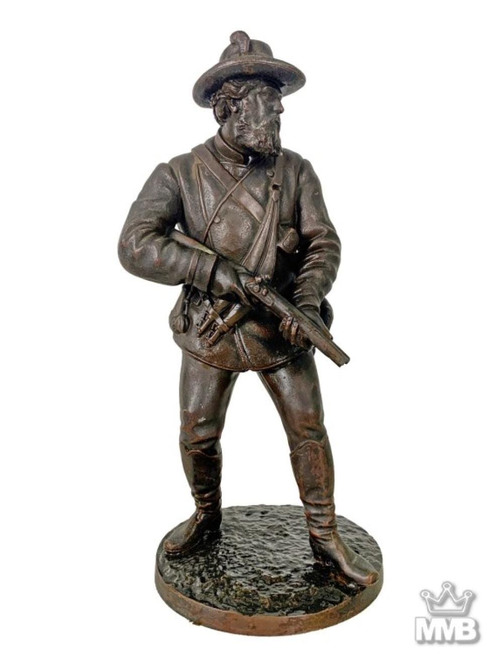 Bronze-toned armed soldier sculpture standing with a long rifle, wearing a hat and coat, on a round textured base.