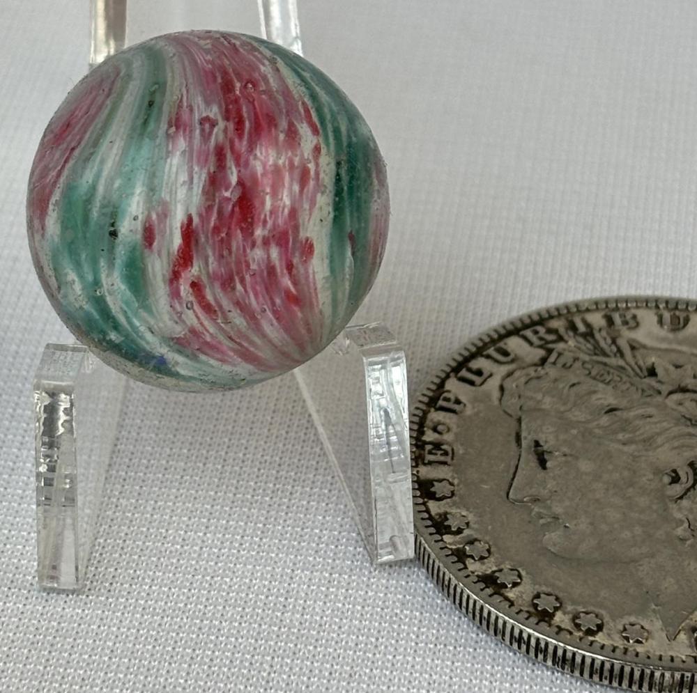 Close-up of a round glass marble on a clear stand, with green and red swirled pattern and a faint white core.