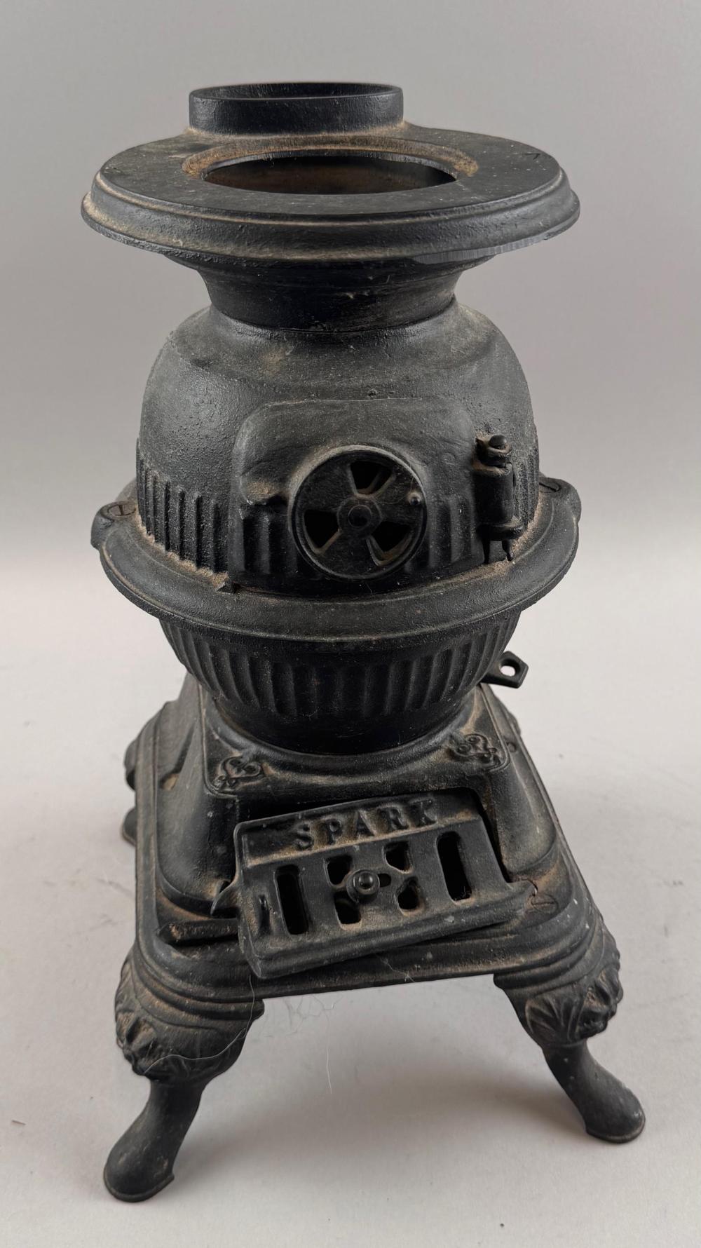 Small black cast-iron potbelly stove with a round firebox door and a circular grate opening, standing on four legs.