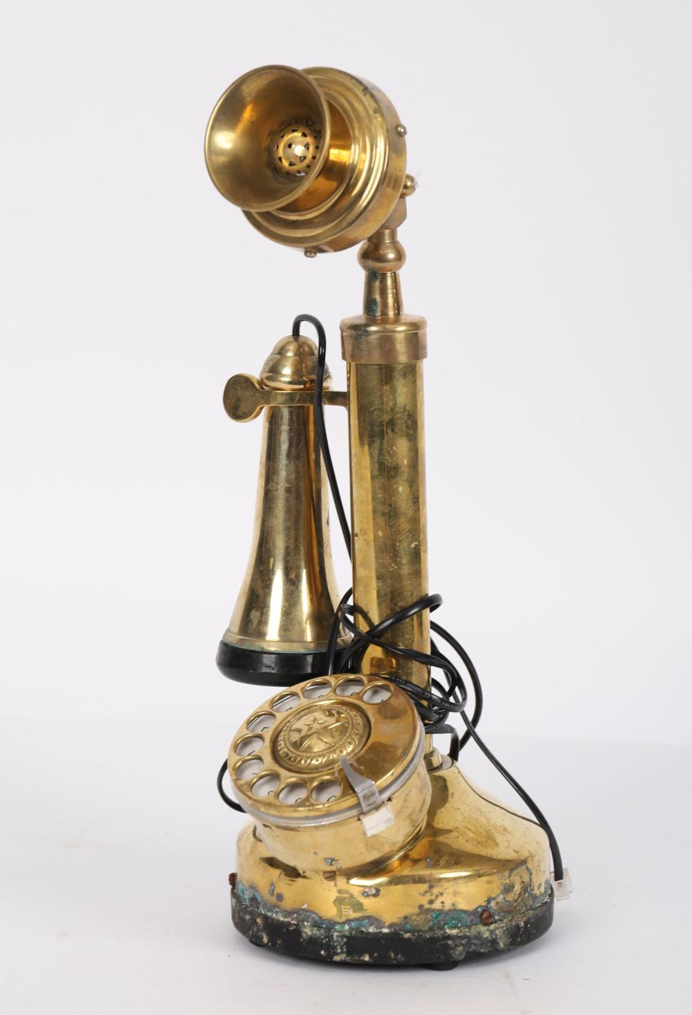 Vintage brass candle-holder shaped telephone with rotary-style dial and black cord base, photographed on a white background.