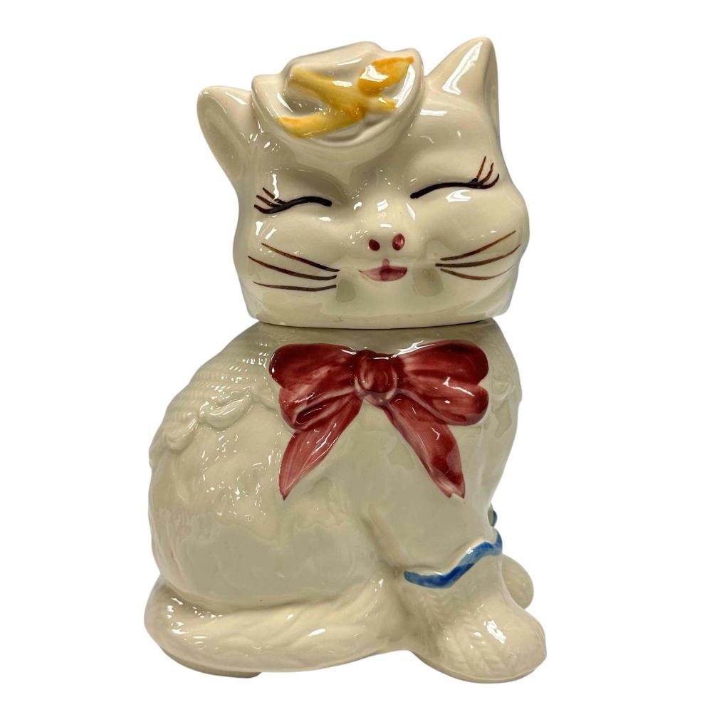 Cream-colored cat cookie jar with painted face, red bow at the neck, and yellow hat-like top on a white background.
