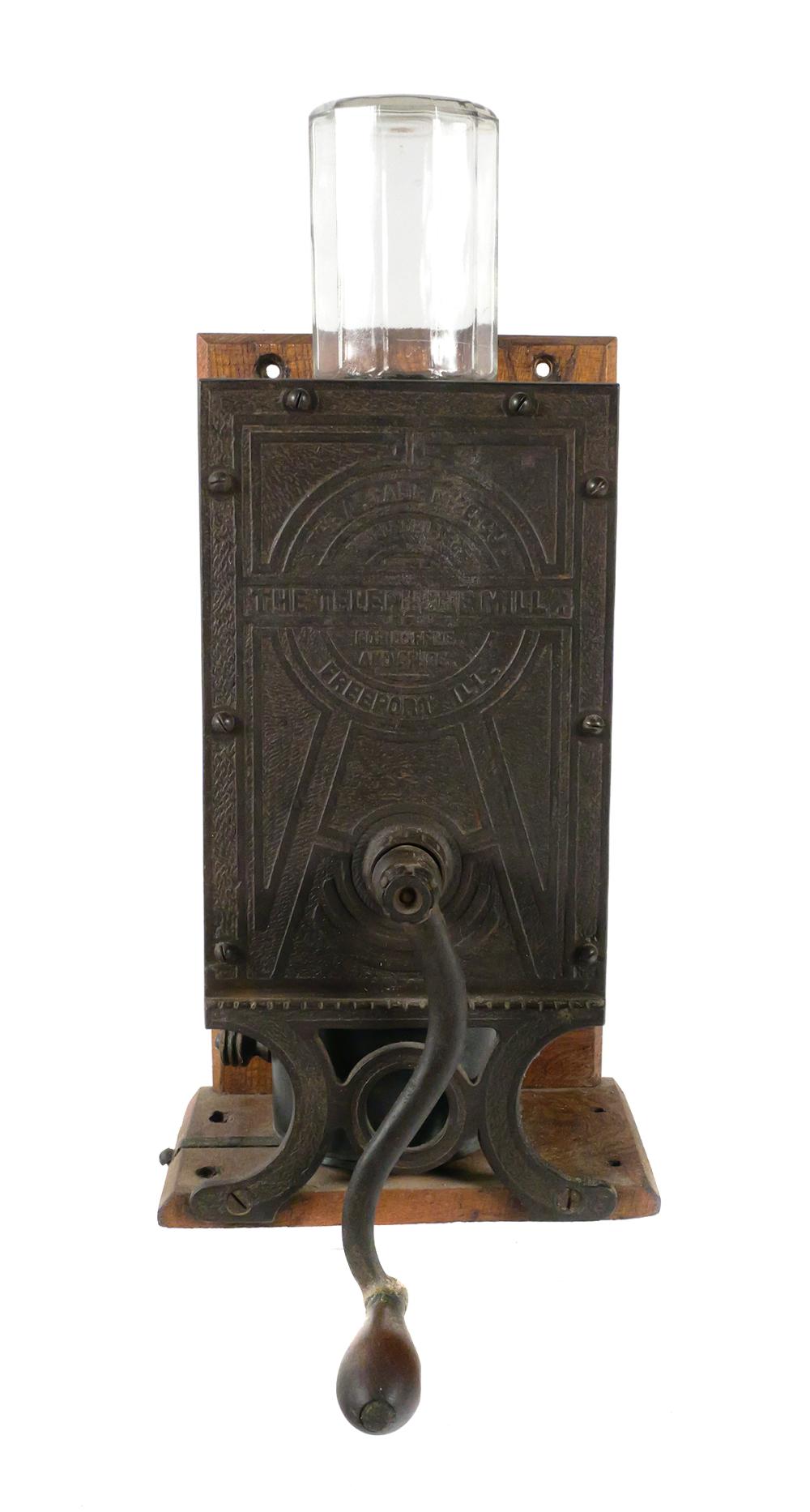 Antique-style coffee grinder with a clear glass cylinder on top and a dark metal front panel, sitting on a wooden base.