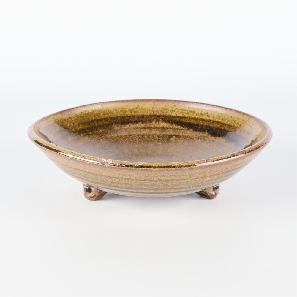 Glazed ceramic tripod bowl with a shallow round basin, tan body, and dark speckled interior ring and rim.