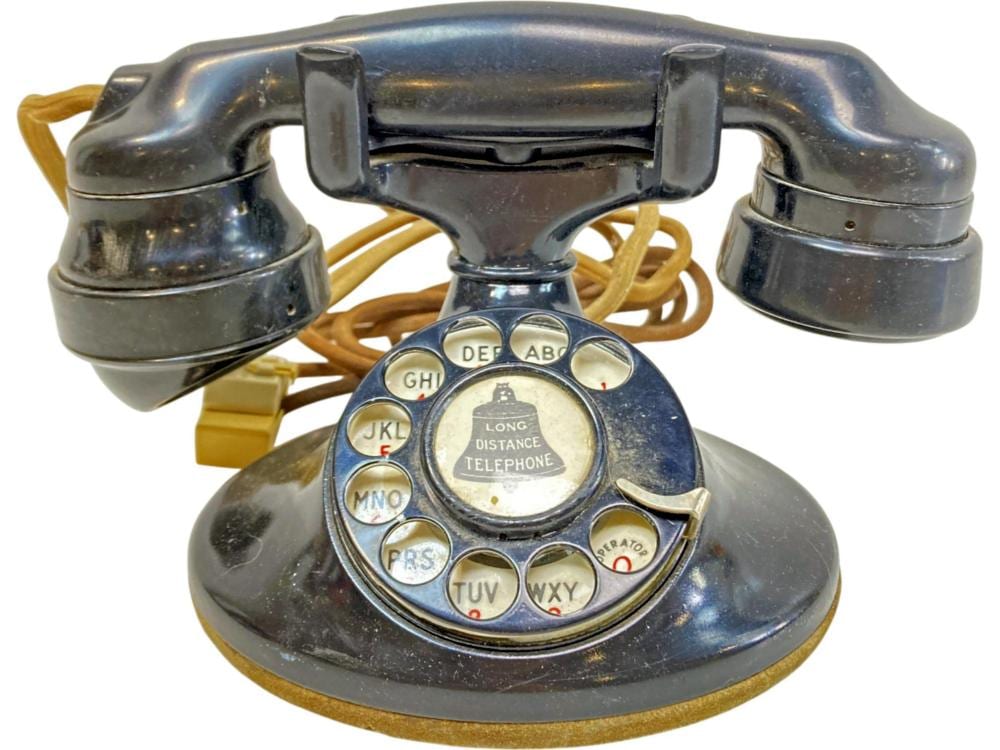 Vintage rotary dial desk telephone with dark handset and blue base, showing lettered number dial and “LONG DISTANCE TELEPHONE” label.