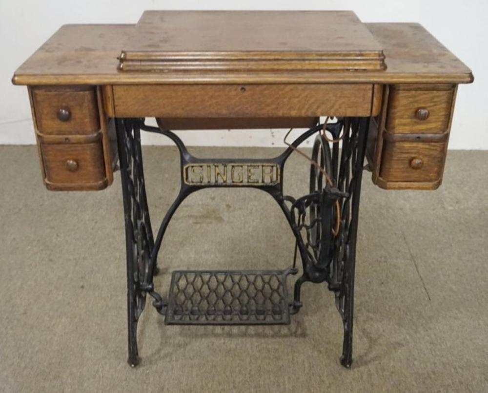 Antique wooden treadle sewing machine cabinet with the black iron machine frame and front foot treadle visible.