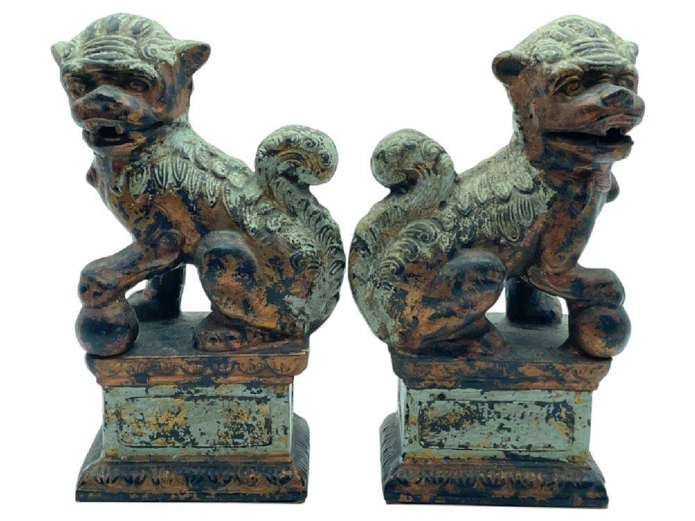 Pair of small Chinese guardian lion (foo dog) figures in green and brown with weathered paint, seated on rectangular bases.
