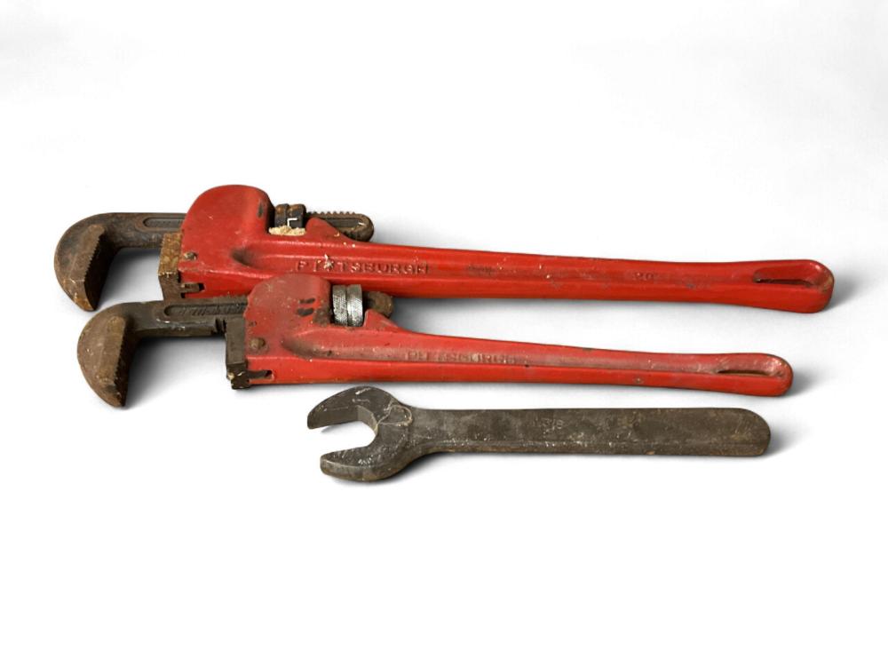 A red pipe wrench tool and a darker open-end wrench laid on a white background.