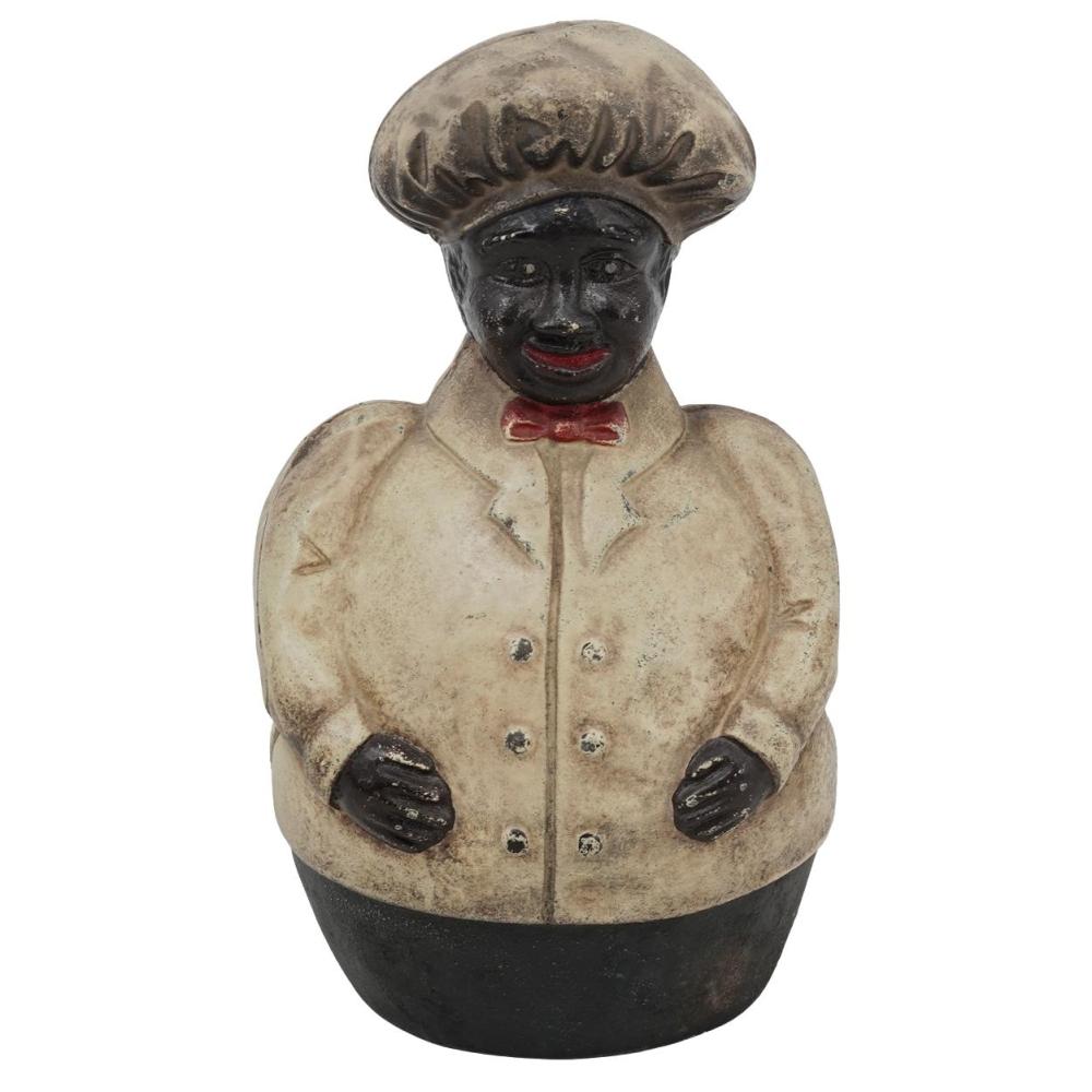 Cast-iron piggy bank figure of a chef wearing a dark hat and a light jacket with a red bow tie, facing forward.