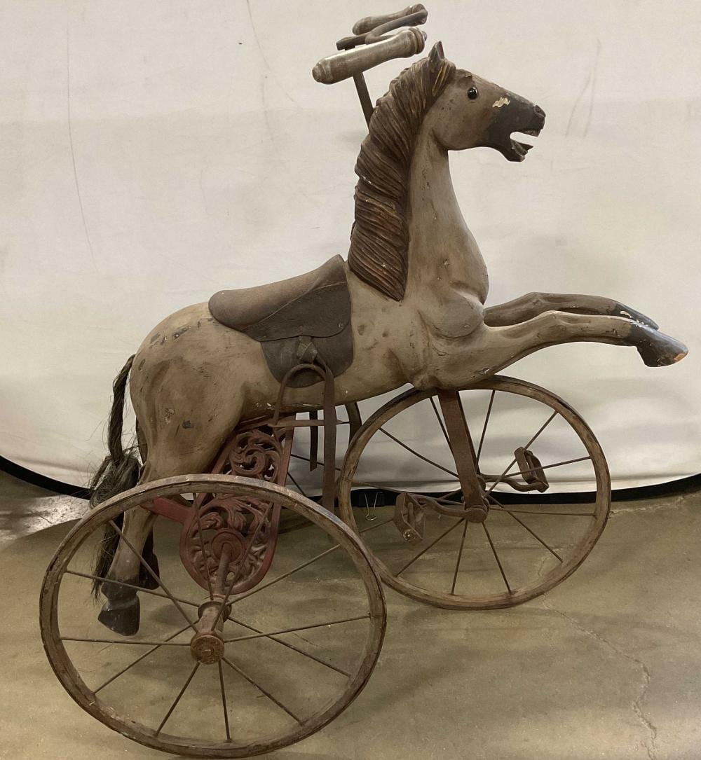Carved wooden horse tricycle with two front wheels and a rider-style saddle, photographed against a light background.